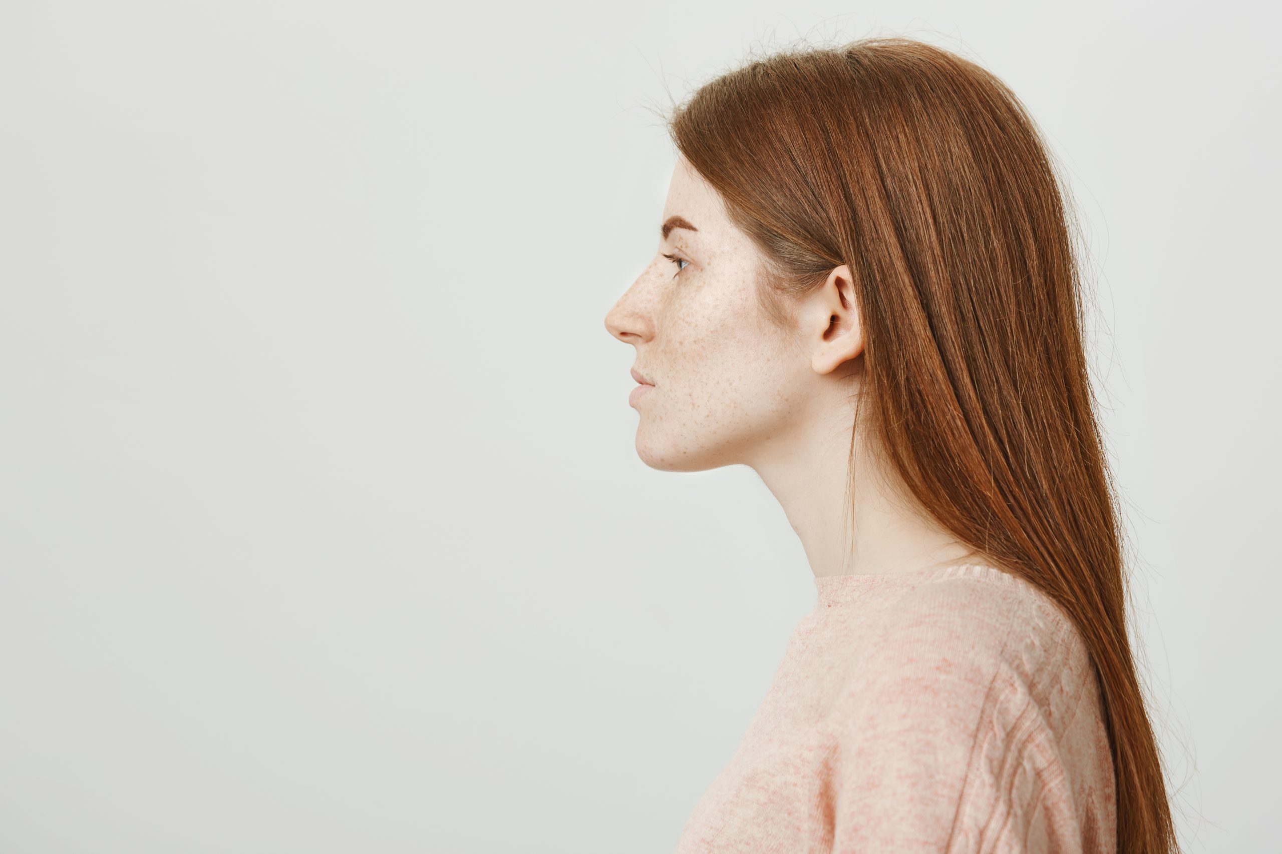 Profile photo of attractive redhead woman with cute freckles looking aside and standing over gray background with calm expression. Young model casts for popular agency